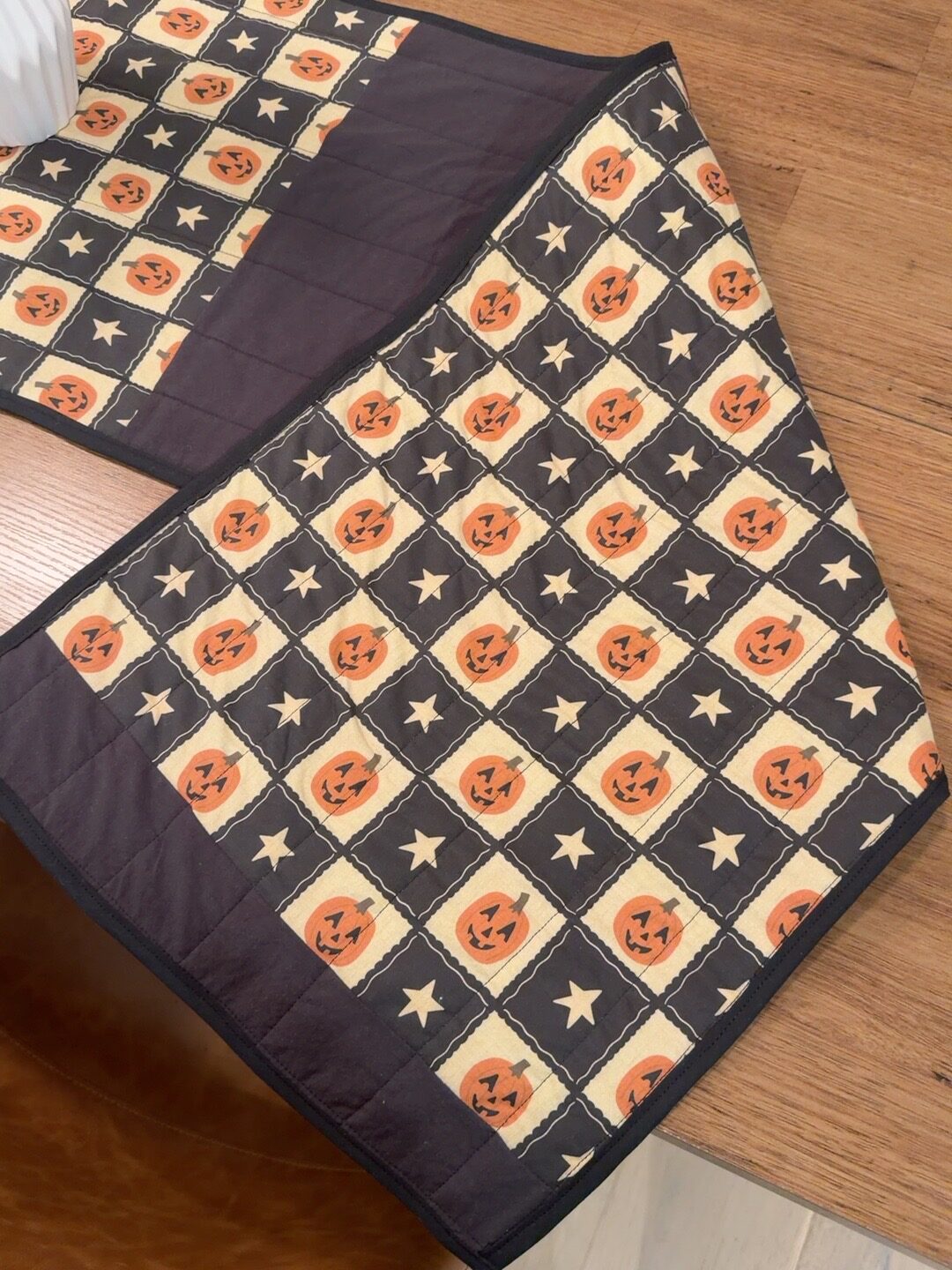The jack o'lantern side of the runner folded back on the table, showing the straight line quilting and black bias tape binding